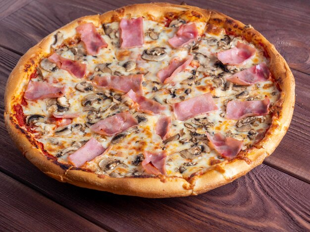 Zbliżenie pizza z szynką i pieczarkami na brązowym drewnianym tle Tradycyjne włoskie danie Pyszne i niezdrowe danie Widok z góry płaski lay