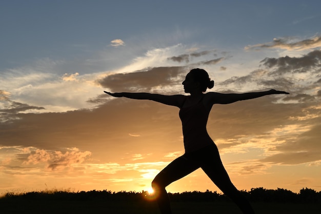 Zbliżenie podświetlanej młodej kobiety ćwiczącej jogę podczas wschodu słońca