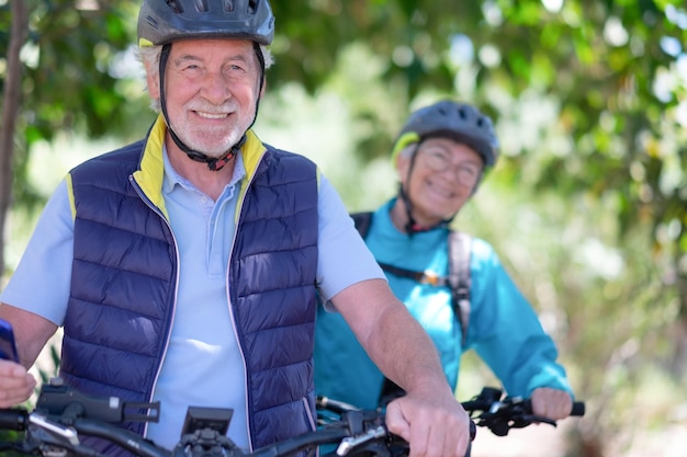 Zbliżenie portret aktywnej pary seniorów rasy kaukaskiej z rowerami elektrycznymi biegającymi na zewnątrz w parku Dwóch uśmiechniętych seniorów w kasku rowerowym, ciesząc się zdrowym stylem życia w przyrodzie