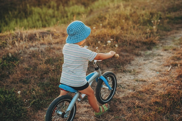 Zbliżenie portret dziecka jazda na rowerze na drodze w letni wieczór na sobie niebieski kapelusz widok z tyłu