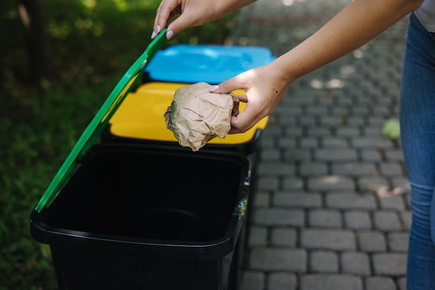 Zdjęcie zbliżenie portret kobiety ręka rzucająca zmiętą papierową torbę w recyklingu kosza na zewnątrz kosze do recyklingu
