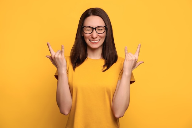 Zbliżenie Portret ładna Brunetka Włosy Pani Pokazuje Rock'n'roll Punk Znak, Sprawia, że Gest Zwycięzcy, Na Białym Tle Na żółtym Tle, Kopiować Miejsca Na Tekst. Koncepcja Miłości Muzyki. świętujemy Zwycięstwo, Sukces