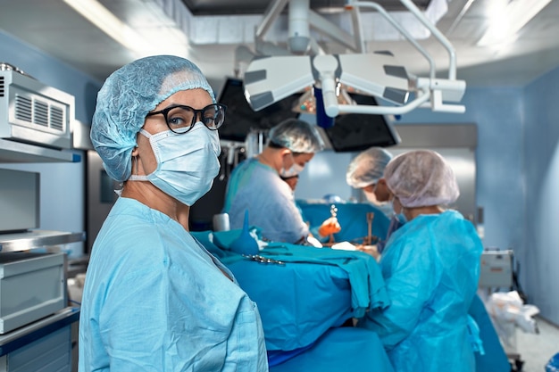 Zbliżenie portret lekarki w okularach i masce na tle zespołu chirurgów duri