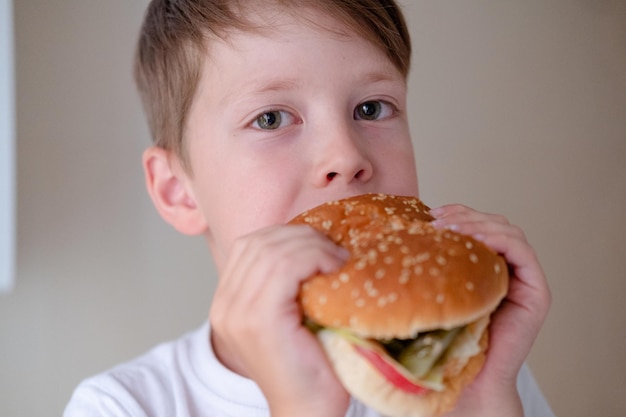 Zbliżenie portret małego chłopca jedzącego ogromnego burgera na białym tle