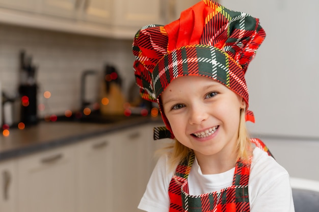 Zbliżenie portret małej szczęśliwej uśmiechniętej blondynki w stroju kucharza w kuchni