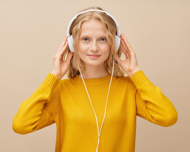Zbliżenie portret młodej kobiety słuchania muzyki w słuchawkach na beżowej ścianie