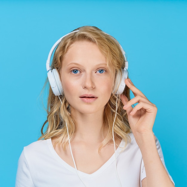 Zbliżenie portret młodej kobiety słuchania muzyki w słuchawkach na jasny niebieski odcień