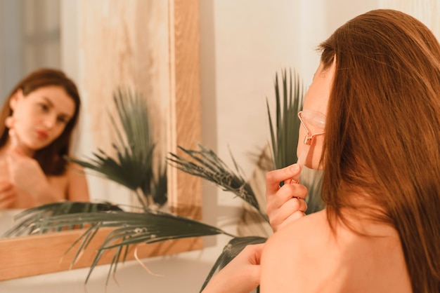 Zdjęcie zbliżenie portret pięknej brunetki za pomocą jadeitowego masażu rolkowego do masażu twarzy z drenażem limfatycznym pielęgnacja skóry i odmładzanie