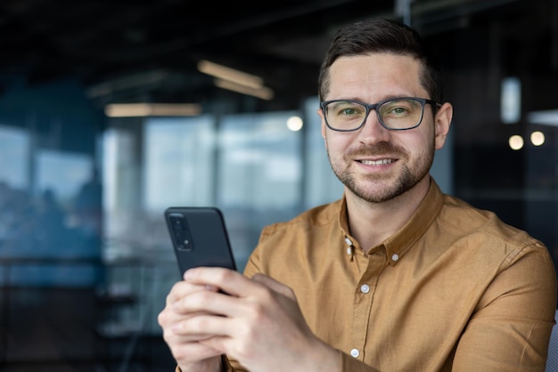 Zbliżenie portret programisty z telefonem mężczyzna w koszuli w miejscu pracy uśmiecha się i patrzy