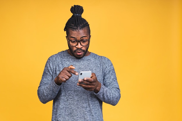 Zbliżenie Portret Przystojny Młody African American Murzyn, Zszokowany, Zaskoczony, Szeroko Otwarte Usta, Szalony Przez To, Co Widzi Na Swoim Telefonie Komórkowym, Na Białym Tle Na żółtym Tle.