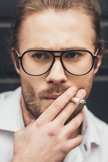 Zbliżenie portret przystojny stylowy młody człowiek w okularach palenia papierosów