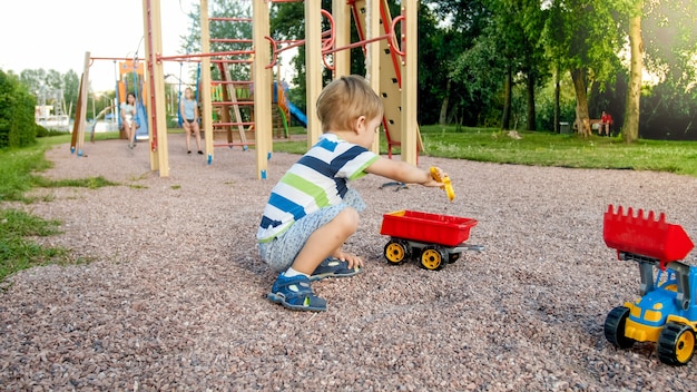 Zbliżenie portret szczęśliwy uśmiechający się 3-letni chłopiec dziecko kopiący piasek na placu zabaw z zabawkową ciężarówką z tworzywa sztucznego lub koparki