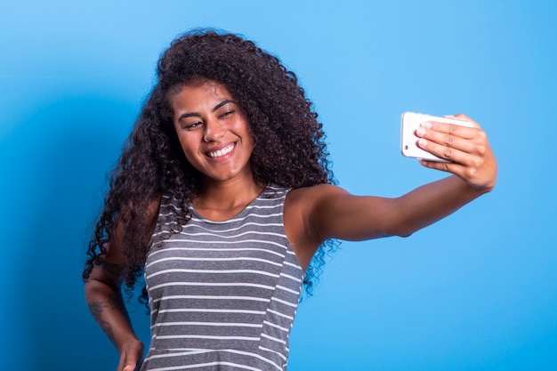 Zbliżenie portret uśmiechnięta młoda atrakcyjna afrykańska brazylijska kobieta trzymając smartfon, biorąc zdjęcie selfie