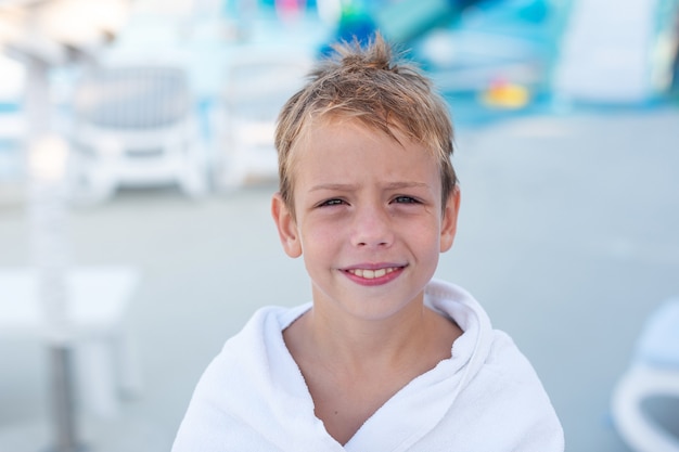 Zbliżenie portret uśmiechniętego chłopca owiniętego w ręcznik po kąpieli w odkrytym basenie
