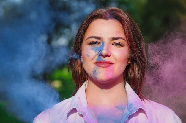 Zbliżenie portret wspaniałej brunetki modelu pozowanie w chmurze różowej i niebieskiej suchej farby Holi