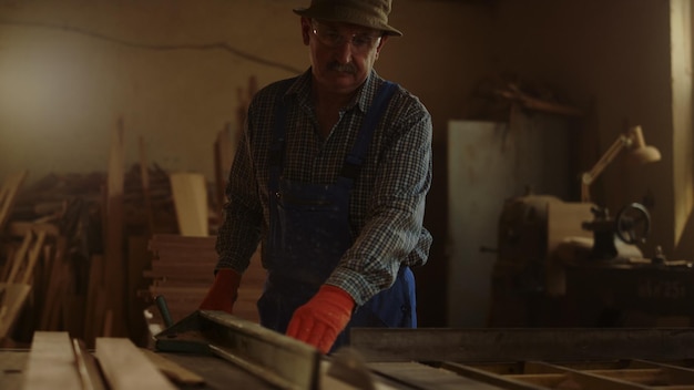 Zbliżenie poważny człowiek pracujący z drewnem w studio Skoncentrowany mężczyzna tnący deski w warsztacie stolarskim w zwolnionym tempie Starszy mężczyzna używający piły w pomieszczeniu