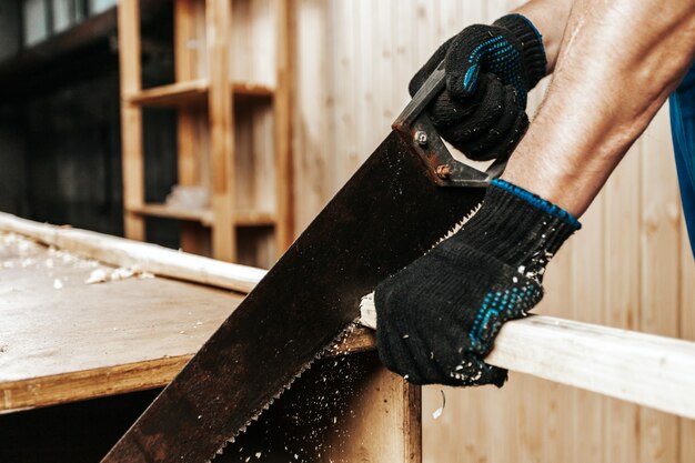 Zbliżenie pracownika budowlanego człowieka piłowanie bloku drewna z ręką Piła w warsztacie