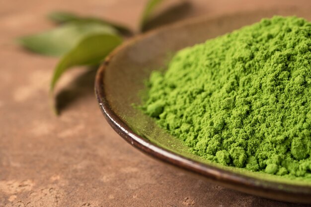 Zbliżenie proszku zielonej herbaty w naczyniu ceramicznym z liściem na stole