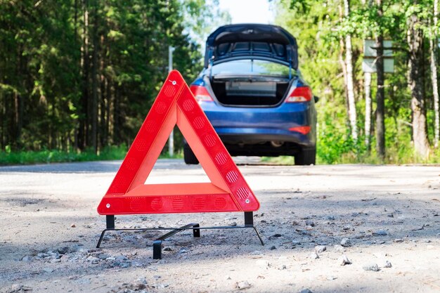 Zbliżenie przenośnego, odblaskowego czerwonego trójkątnego znaku ostrzegawczego na poboczu wiejskiej drogi w pobliżu samochodu Selektywna ostrość