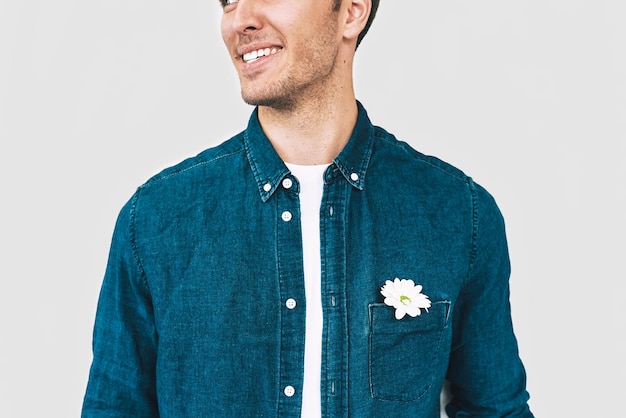 Zbliżenie przycięte portret przystojny mężczyzna uśmiechający się i noszący niebieską koszulę dżinsową z białym kwiatem w kieszeni pozowanie na białej ścianie studio Walentynki koncepcja dzień matki