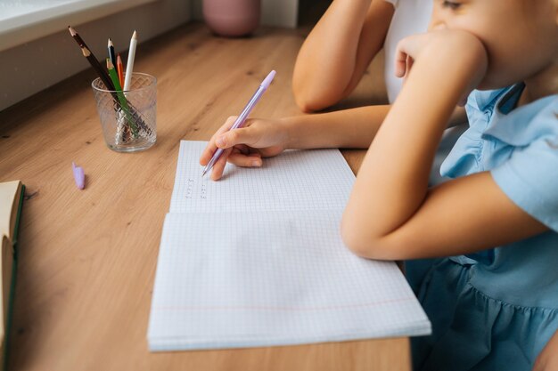 Zbliżenie przycięte zdjęcie podstawowej córki odrabiania lekcji pisania w zeszycie z piórem z młodymi