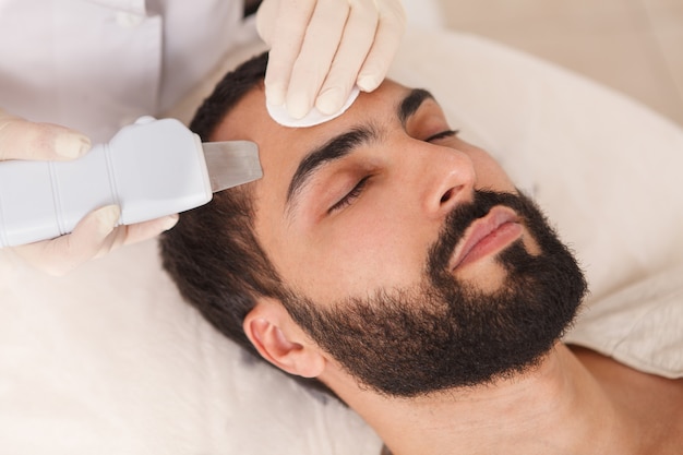 Zbliżenie przystojny brodaty mężczyzna coraz oczyszczanie ultradźwiękowe przez kosmetologa