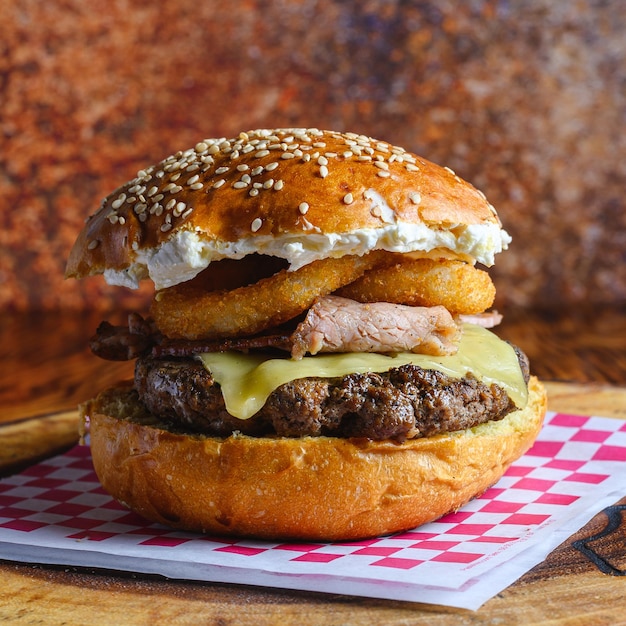 Zbliżenie pysznego burgera wołowego z krążkami cebuli na stole z rozmytym tłem