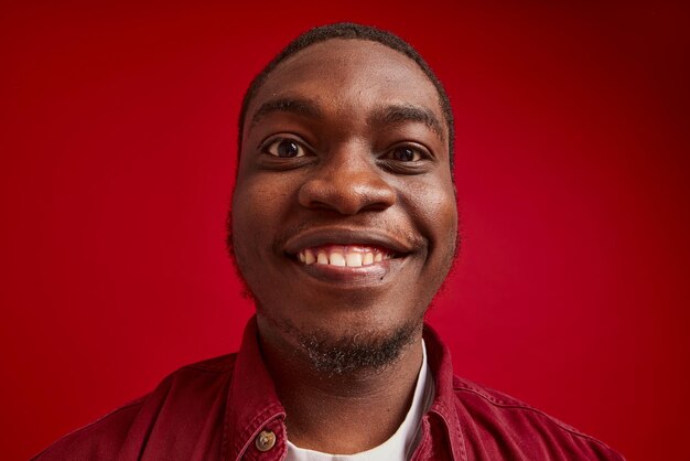 Zbliżenie radosnego młodego Afroamerykanina ze słuchawkami bezprzewodowymi odizolowanymi na czerwono