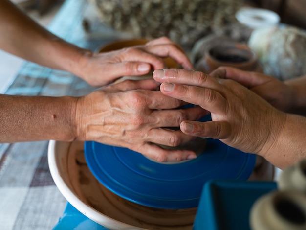 Zdjęcie zbliżenie rąk dwóch kobiet uprawiających ceramikę, jedna ucząca się drugiej na kołku uprawiającym ceramikę