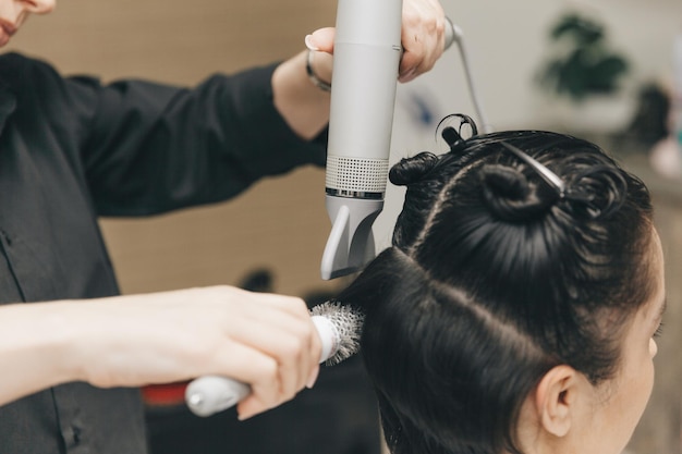 Zbliżenie rąk fryzjera suszącego włosy kobiet suszarką do włosów z krótką fryzurą i stylizacją