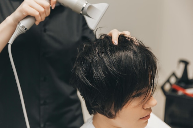 Zbliżenie rąk fryzjera suszącego włosy kobiet suszarką do włosów z krótką fryzurą i stylizacją
