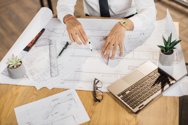 Zbliżenie rąk inżyniera architekta lub projektanta siedzącego przy stole i analizującego plany
