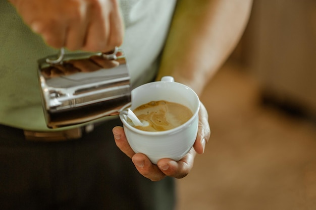 Zbliżenie rąk nalewa mleko i przygotowuje świeże cappuccino