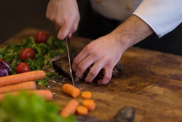 zbliżenie rąk szefa kuchni w kuchni hotelowej lub restauracyjnej przygotowującej stek wołowy z dekoracją warzywną