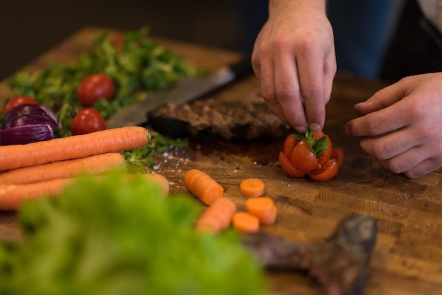 zbliżenie rąk szefa kuchni w kuchni hotelowej lub restauracyjnej przygotowującej stek wołowy z dekoracją warzywną