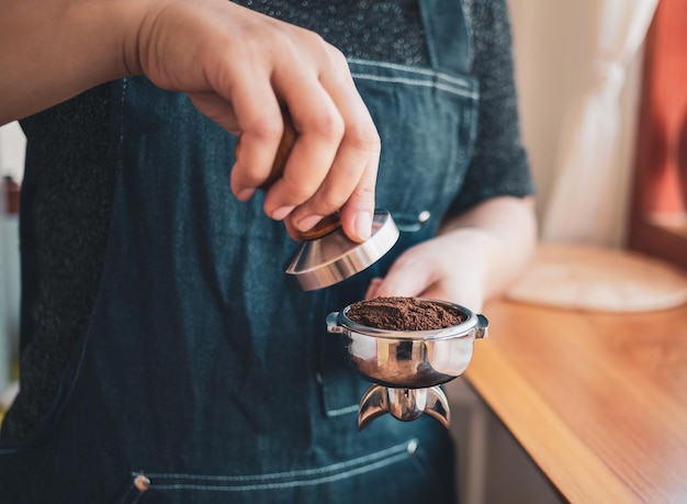 Zbliżenie ręcznego baristy lub ekspresu do kawy trzymającego portafilter i ubijak do kawy robiący espresso