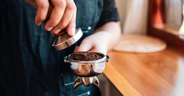 Zbliżenie ręcznego baristy lub ekspresu do kawy trzymającego portafilter i ubijak do kawy robiący espresso