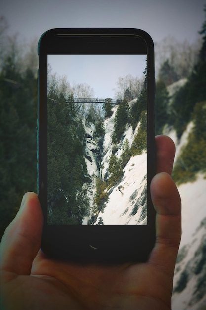 Zdjęcie zbliżenie ręcznego fotografowania pokrytych śniegiem gór za pomocą telefonu komórkowego