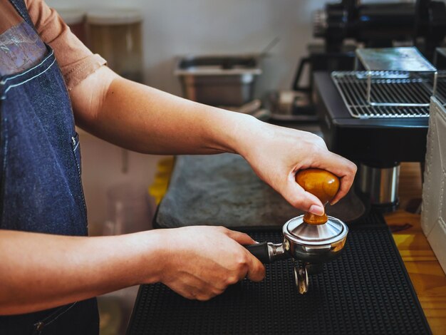 Zdjęcie zbliżenie ręcznej kawiarni barista robiącej kawę za pomocą ręcznej prasy kawy mielonej za pomocą tamper