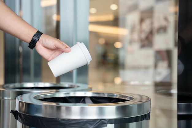 Zbliżenie ręka mężczyzny rzucającego pustą papierową filiżankę kawy do kosza na śmieci