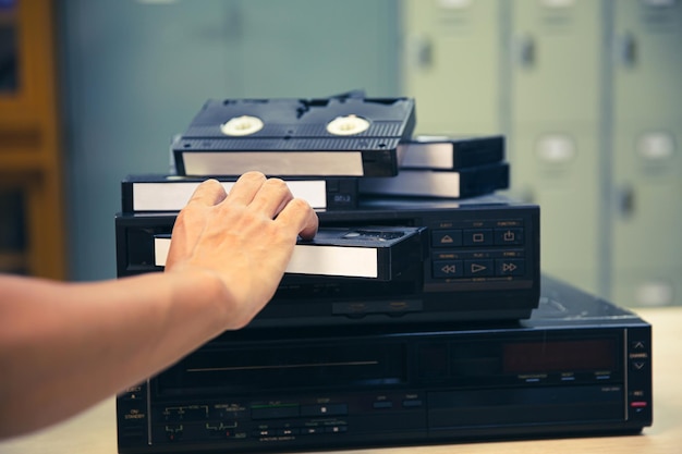 Zbliżenie ręka wybiera i wkłada lub wkłada kasetę wideo VHS na odtwarzacz taśmowy koncepcja stylu retro lub vintage urządzenia elektryczne i elektroniczne urządzenie do odtwarzania multimediów w starym stylu