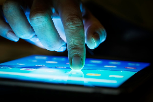 Zbliżenie ręki dotykającej telefonu komórkowego w ciemni