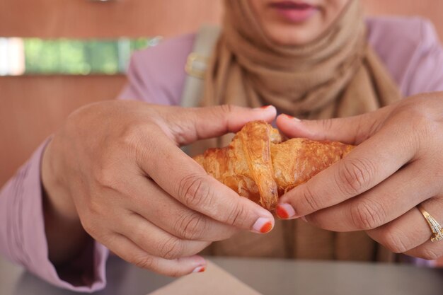 Zbliżenie ręki łamiącej bułeczkę croissant