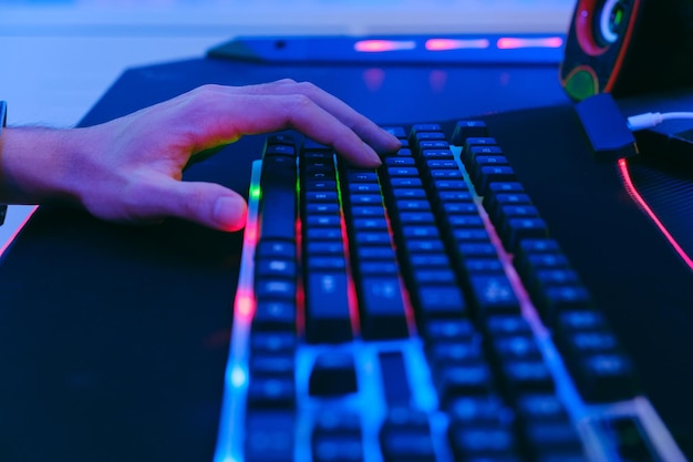Zbliżenie ręki profesjonalnego gracza e-sportowego i mechanicznej klawiatury push z neonowym światłem na dużej podkładce pod mysz na stole komputerowym Profesjonalny sprzęt dla graczy