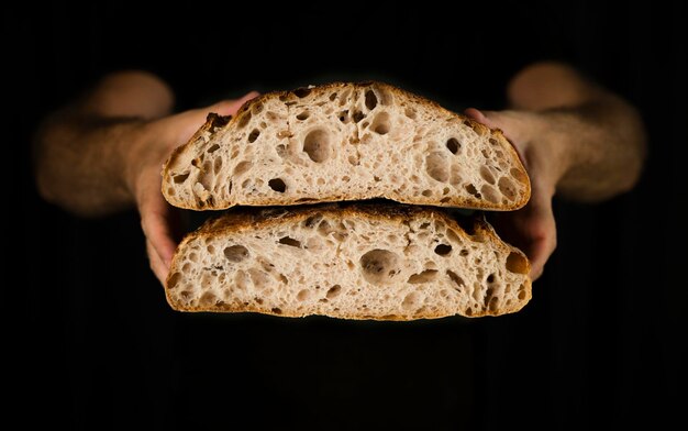 Zdjęcie zbliżenie ręki trzymającej chleb połowicznie pocięty na czarnym tle