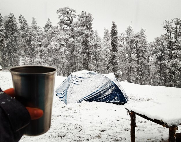 Zdjęcie zbliżenie ręki trzymającej filiżankę kawy w namiocie na pokrytym śniegiem polu zimą