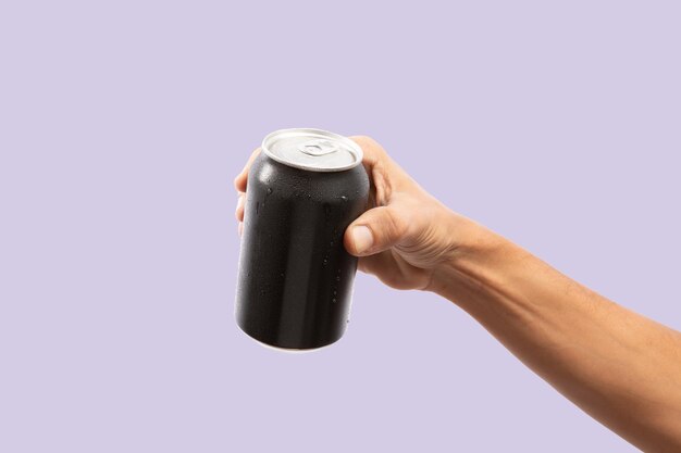 Zdjęcie zbliżenie ręki trzymającej pustą puszkę aluminiową z kondensacją izolowaną na fioletowym