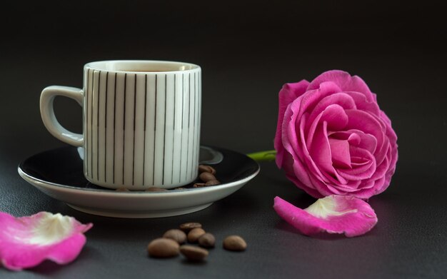 Zdjęcie zbliżenie różowej róży i filiżanki kawy na stole na czarnym tle