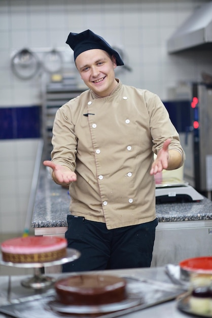 Zbliżenie skoncentrowanego męskiego cukiernika dekorującego deserowe ciasto w kuchni