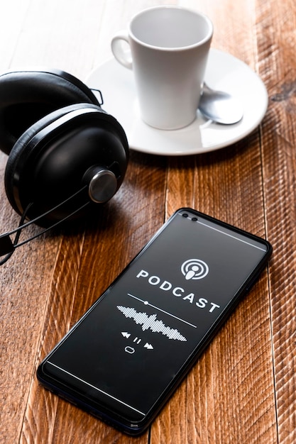 Zdjęcie zbliżenie smartfona odtwarzającego podcast ze słuchawkami na stoliku w kawiarni odbiorcy podcastu